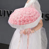 A woman holds a bouquet of pink silk roses wrapped in sheer white fabric.
