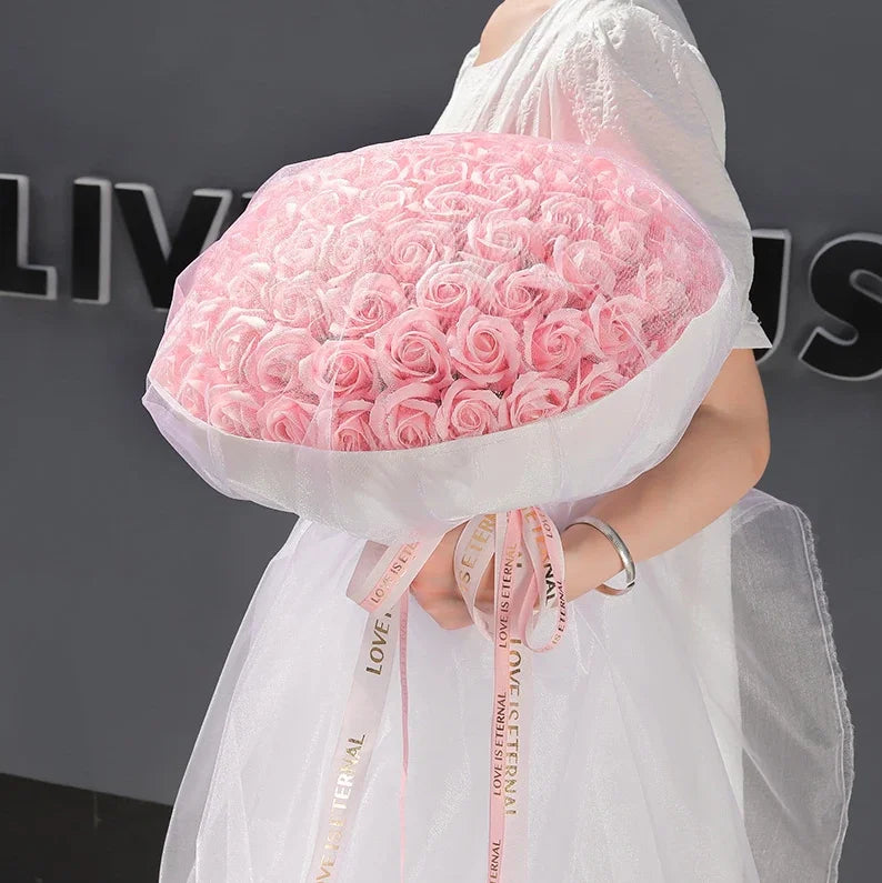 A woman holds a bouquet of pink silk roses wrapped in sheer white fabric.