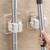 A close-up of a silver adhesive wall hook designed to hold mops and brushes, mounted on a wall.