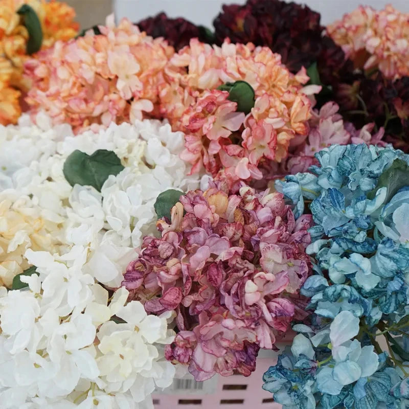 A close-up display of various colored silk hydrangea stems in shades of peach, pink, white, and blue.