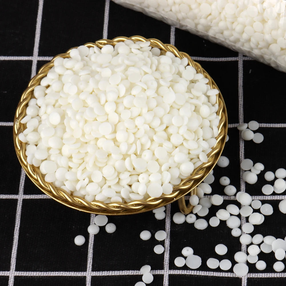 A golden bowl filled with white soy wax flakes is shown on a black and white checkered surface.