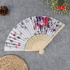 A hand carved bamboo folding fan with purple and pink floral patterns displayed on a gray surface.