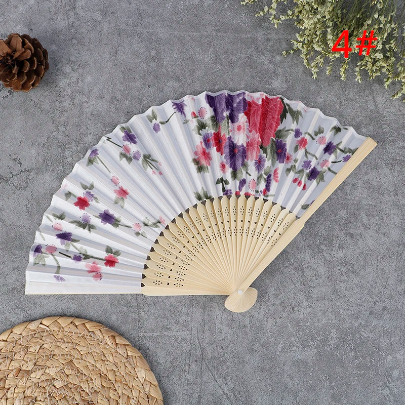 A hand carved bamboo folding fan with purple and pink floral patterns displayed on a gray surface.