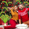 A smiling couple in festive red clothing posing with a decorated Christmas tree.