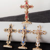 Three gold metal crucifix desk crosses with self-adhesive bases displayed on a dark surface.