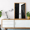 A modern architecture canvas wall art featuring a tall skyscraper silhouette framed in wood on a white shelf.