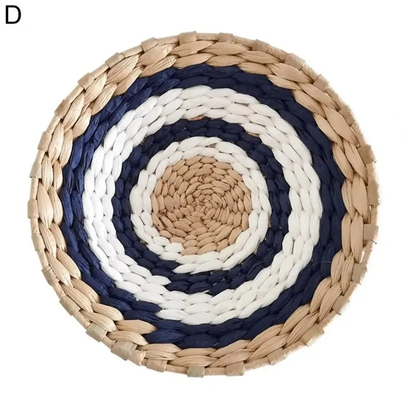Round woven straw wall decor hanging featuring concentric rings of white, dark blue, and natural straw colors.