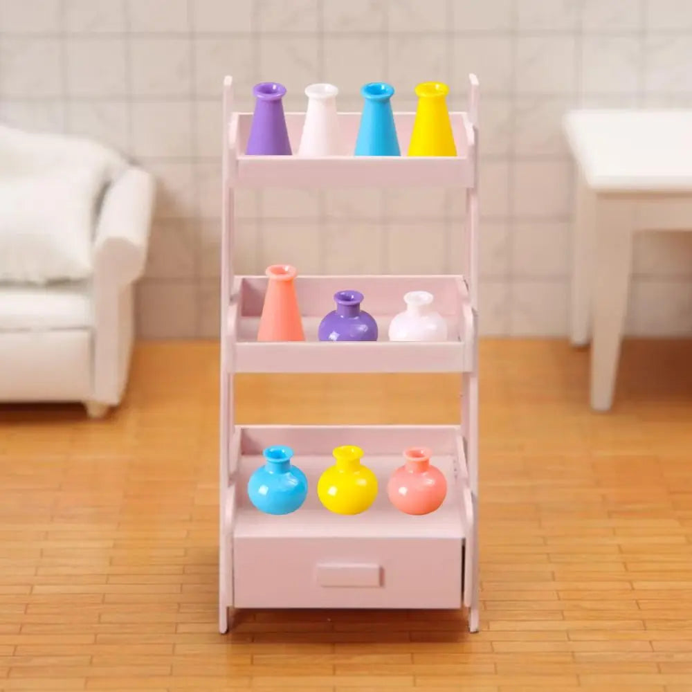 A pink tiered shelf display of colorful miniature resin vases for dollhouse decor.