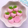 Pink strawberry resin flatback charms with green leaves displayed in a white dish.