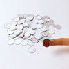 A hand is holding a pile of round silver mirror tiles against a white background.