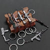 A collection of realistic miniature alloy gun models and various metal keychains displayed on a wooden surface.