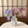 A hand-painted blue and white porcelain vase holds purple flowers on a white table.