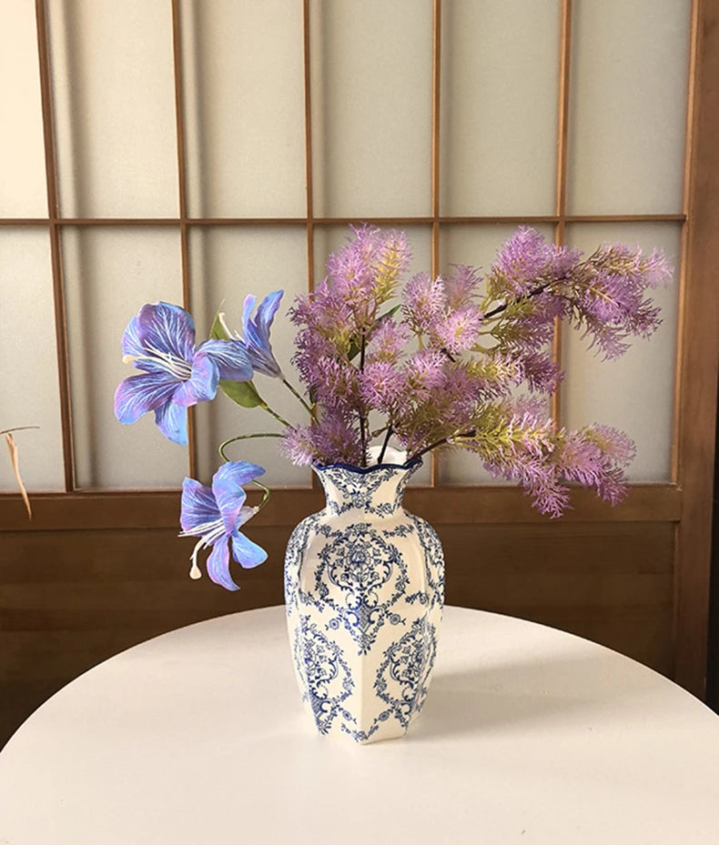 A hand-painted blue and white porcelain vase holds purple flowers on a white table.