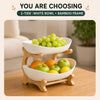 A two-tier fruit basket stand featuring a white bowl and bamboo frame holding green grapes and yellow apples.
