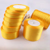 A stack of gold yellow satin ribbon rolls and a single large roll of the same ribbon.