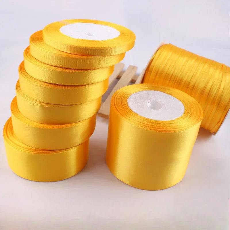 A stack of gold yellow satin ribbon rolls and a single large roll of the same ribbon.