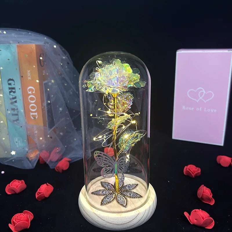 A glass dome containing a crystal rose flower rests on a wooden base, next to a bag of crystals and red rose petals.