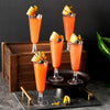 A display of orange cocktail drinks in elegant disposable champagne glasses garnished with citrus peels and berries.