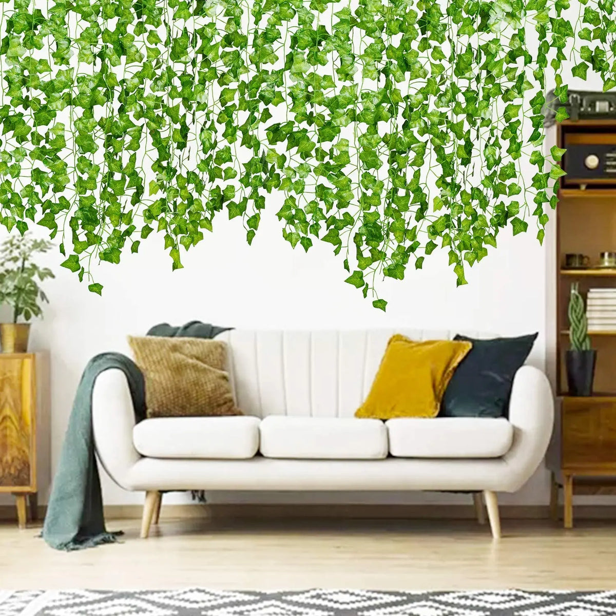 A white sofa decorated with yellow and dark blue pillows beneath a lush green artificial ivy garland hanging from the ceiling