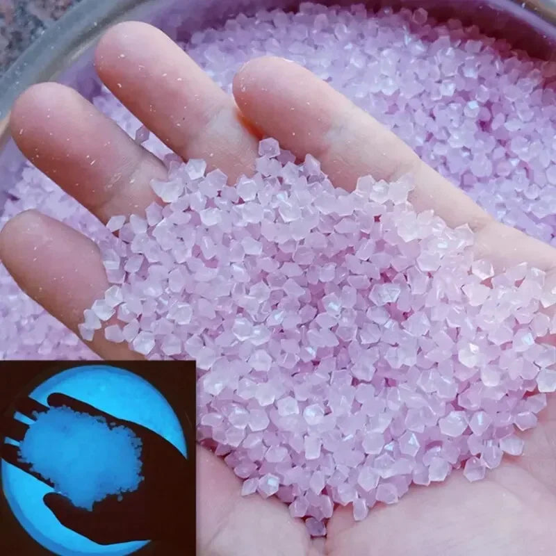 A hand holds a pile of luminous pink glow-in-the-dark pebbles for garden and aquarium decor.