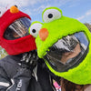 A person wearing a bright lime green cartoon plush helmet cover for a full-face motorcycle helmet.