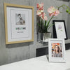 A framed photo with the word WELCOME displayed on a light wooden frame, next to a potted pink orchid.