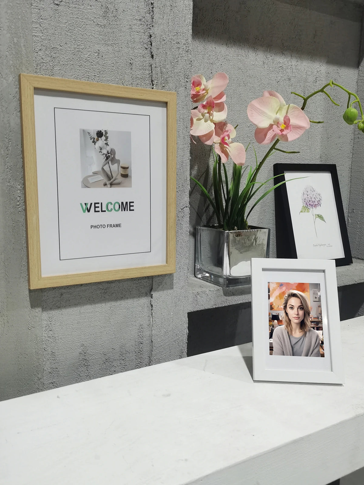 A framed photo with the word WELCOME displayed on a light wooden frame, next to a potted pink orchid.
