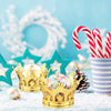 A gold crown sits on a snowy surface next to red and white striped candy canes in a striped cup.