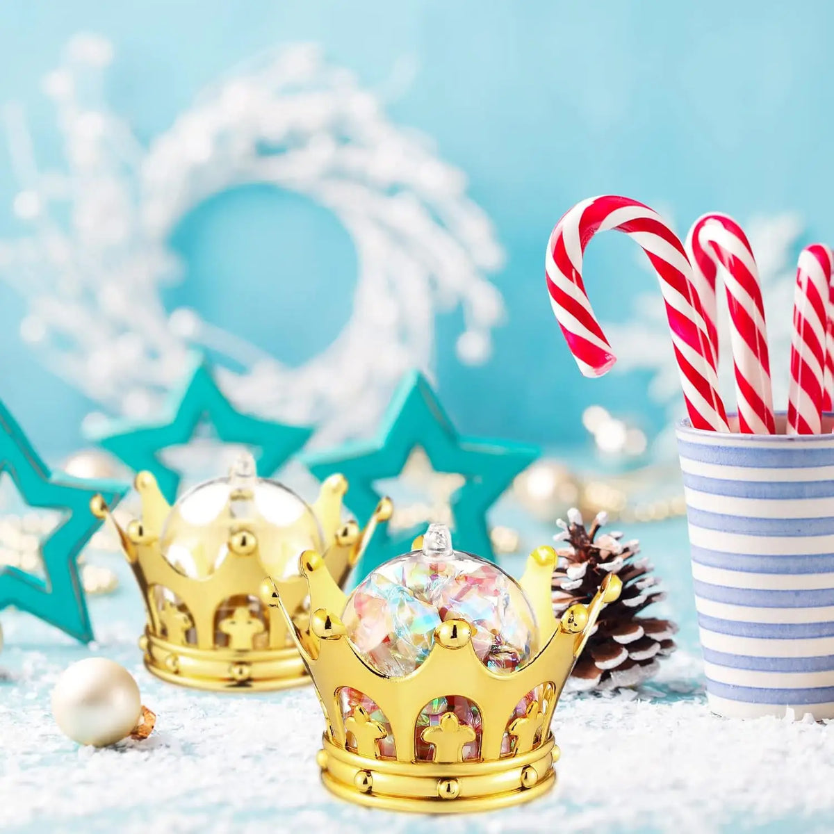A gold crown sits on a snowy surface next to red and white striped candy canes in a striped cup.