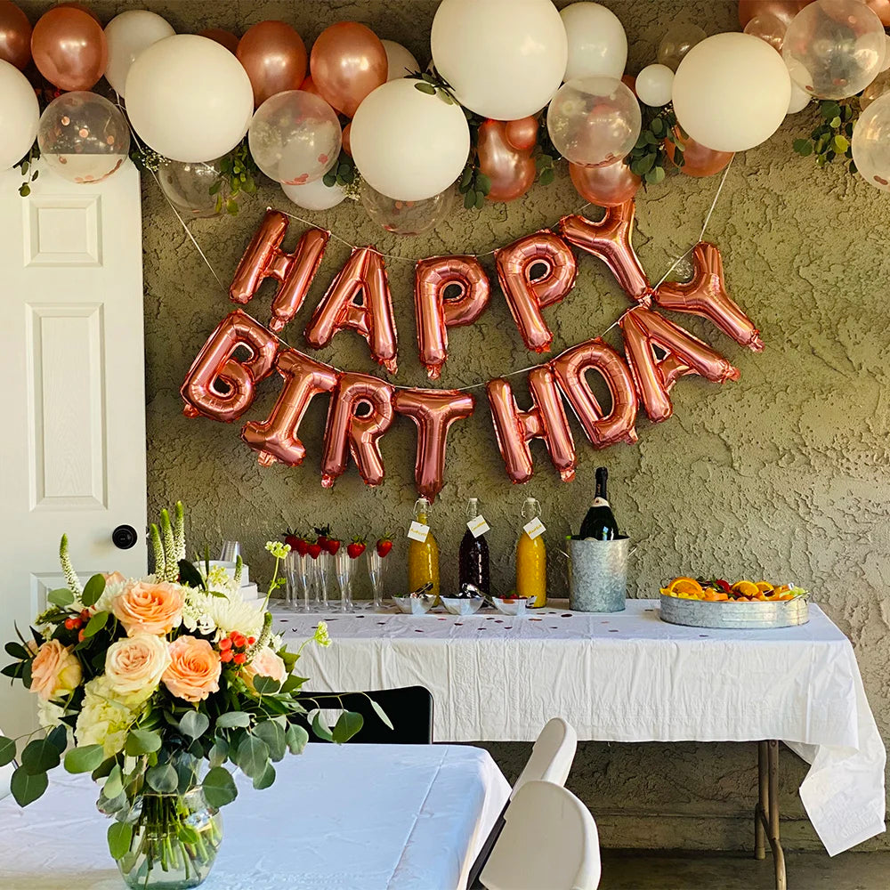 A decorative banner spelling HAPPY BIRTHDAY made of pink and gold foil letter balloons hanging on a textured wall.