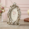 Vintage gold oval resin picture frame with ornate scrollwork displayed on a wooden surface.