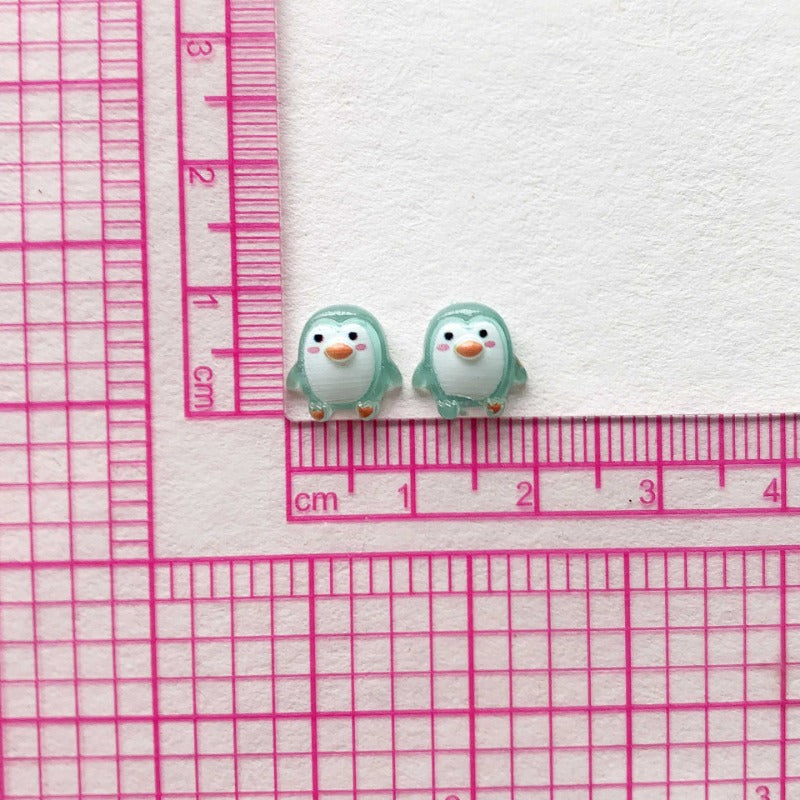 A pair of small, light green resin penguin figurines placed on a pink ruler.