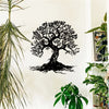 Black silhouette wall art depicting a large tree of life with roots on a white wall next to green plants