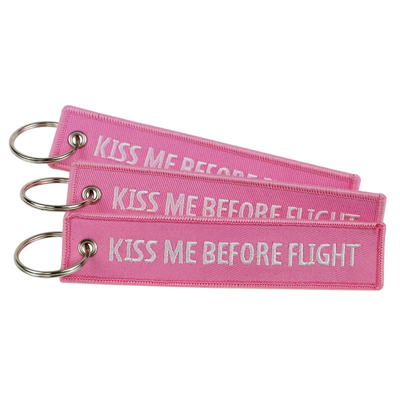 Pink woven keychain tag with the text Kiss Me Before Flight