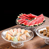 Clear acrylic serving plates filled with sliced watermelon and small appetizers on a wooden table.