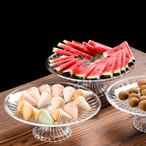 Clear acrylic serving plates filled with sliced watermelon and small appetizers on a wooden table.