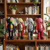 Four stylized bear figurines in various colors and finishes displayed on a wooden shelf.
