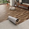 Roll of 3D textured wood grain self-adhesive flooring film laid on a light gray floor.
