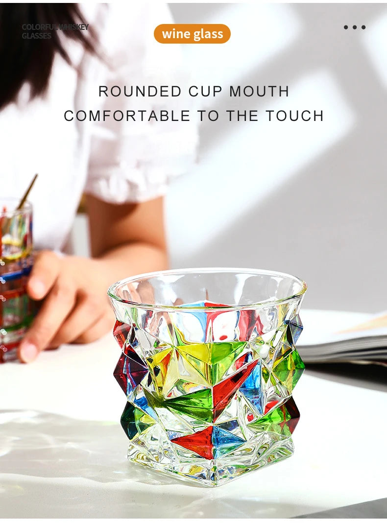 A faceted crystal whiskey glass with colorful geometric cuts is shown on a white surface.