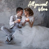 A bride and groom sitting together, looking at each other, illuminated by a glowing neon sign that reads All you need is love