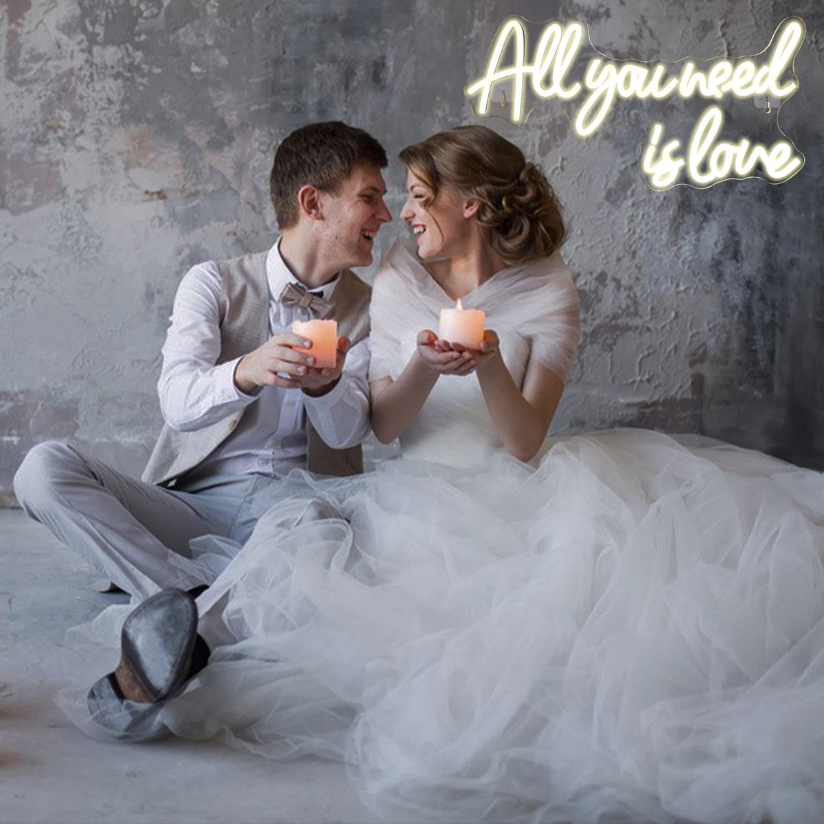 A bride and groom sitting together, looking at each other, illuminated by a glowing neon sign that reads All you need is love