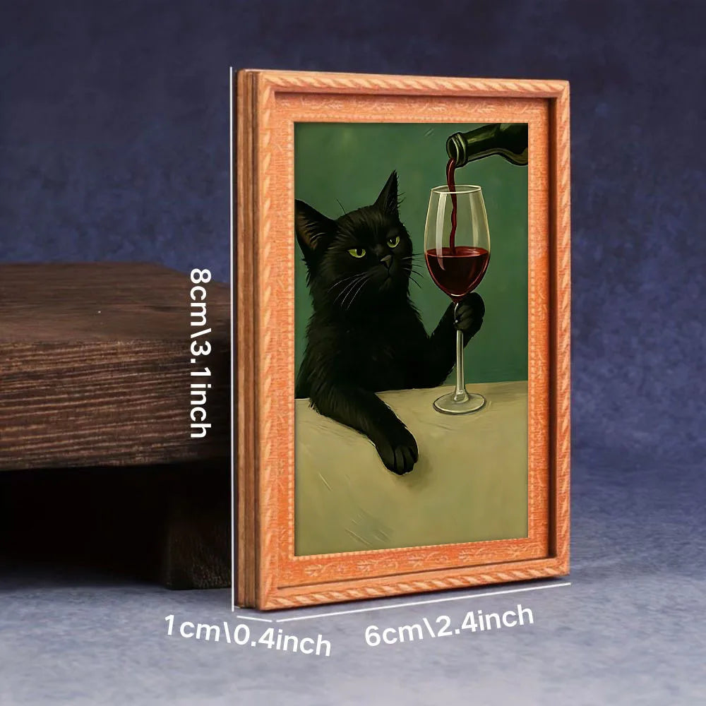 A framed picture of a black cat drinking from a glass of red wine on a green background.