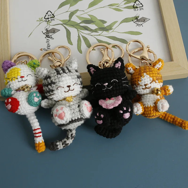 Four handcrafted crochet cat keychain pendants in various colors and textures displayed on a wooden frame.