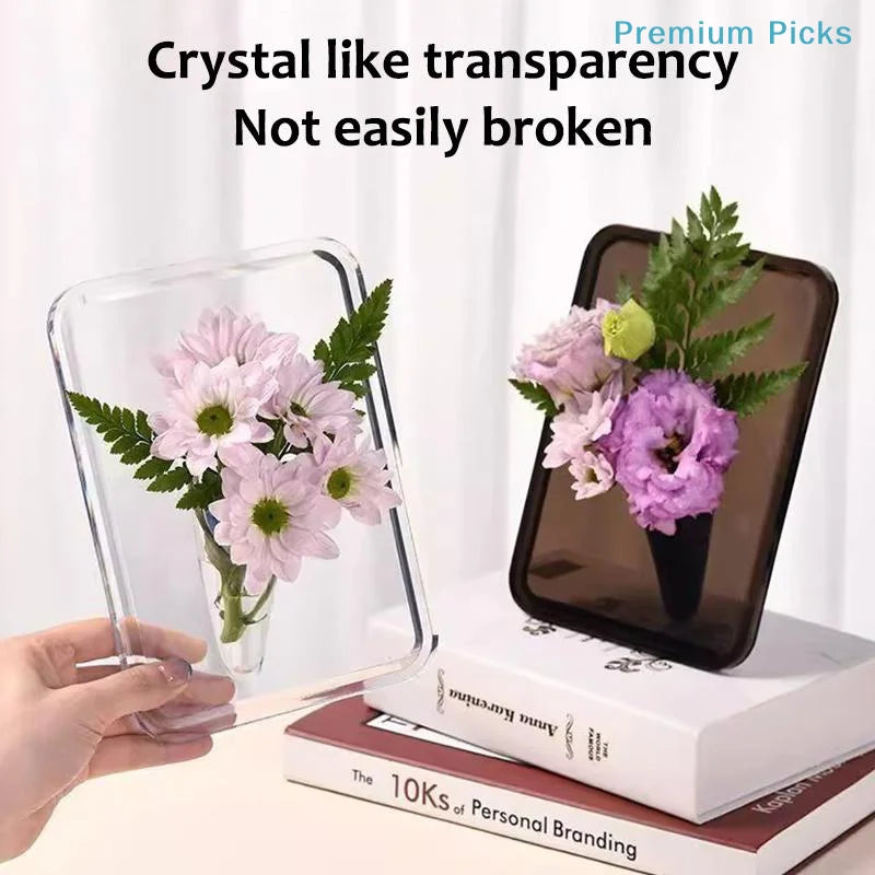 A hand holds a clear acrylic frame flower vase with pink flowers, displayed on a book.