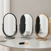 A set of three elegant rotating oval vanity mirrors with silver and gold frames on a white table.