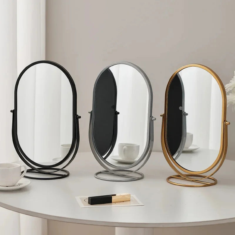 A set of three elegant rotating oval vanity mirrors with silver and gold frames on a white table.
