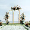 Elegant gold metal wedding arch stand with a floral backdrop on a grassy field.