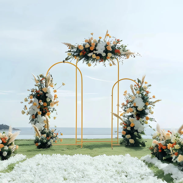 Elegant gold metal wedding arch stand with a floral backdrop on a grassy field.
