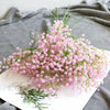 A bouquet of pink artificial gypsophila flowers with delicate green stems displayed on a white surface.