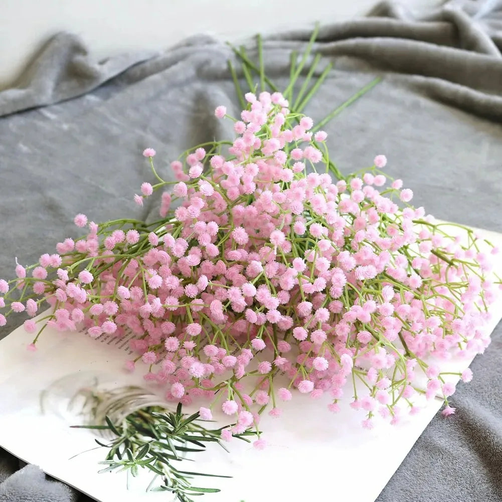A bouquet of pink artificial gypsophila flowers with delicate green stems displayed on a white surface.